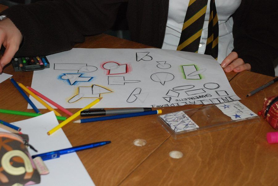 Une feuille d'exercices de géométrie sur une table d'école, entourée de crayons